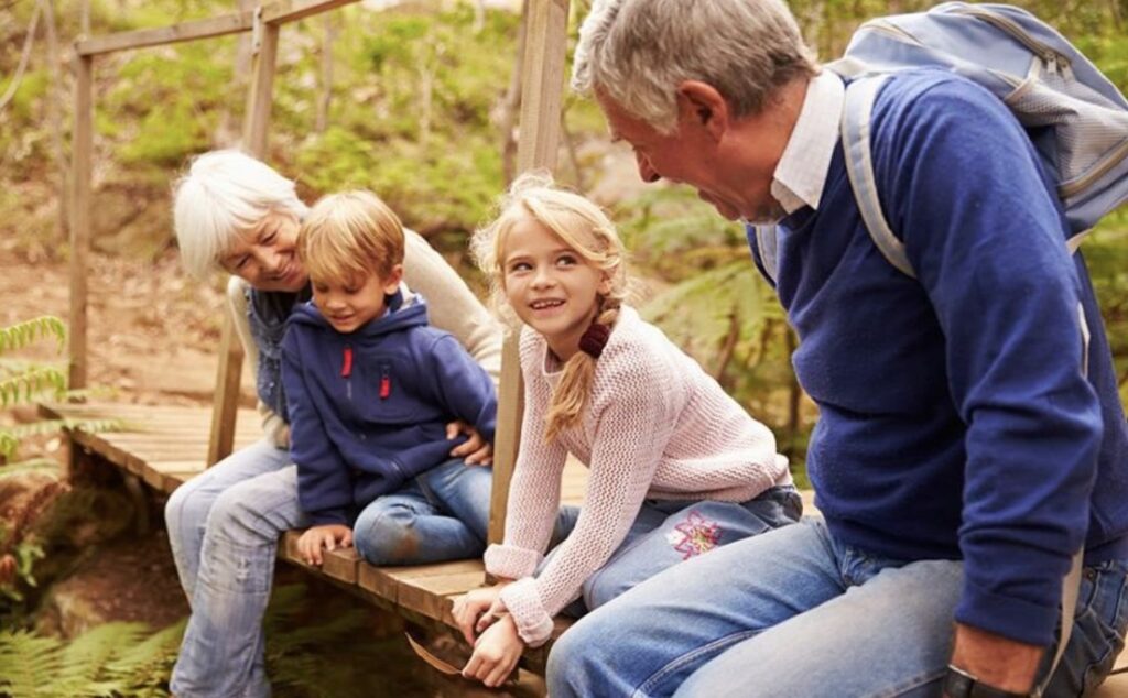 Grandparents sitting on a bridge, talking to their young grandson and granddaughter.